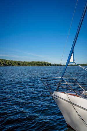 A boat on the shore of a lake surrounded by reed and trees under the blue sky