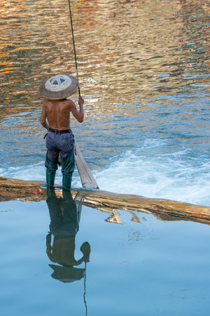 Feng Huang, China -  August 2019 : Fisherman with a traditional triangular chinese hat standing in waters of Tuo river flowing through the centre of Feng huang Old Town and catching fishesのeditorial素材