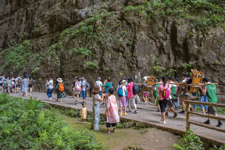 Wulong, China - August 2019 : Tourists carried in a litter on the narrow mountain trekking path in the gorge valley among karst limestone rock formations, Wulong National Parkのeditorial素材