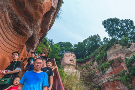 Leshan, China - July 2019 : Crowds of tourists walking down the plank walk around Giant  Leshan Buddha monument, a 71-meter tall stone statue built between 713 and 803 during the Tang Dynasty. Located at the confluence of the Minjiang, Dadu and Qingyi rivのeditorial素材