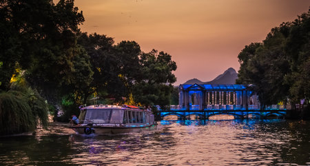 Guilin, China - August 2019 : Sightseeing tour boat ferry carrying tourists sailing in front of Crystal glass bridge on the Shan Lake, Guilin town, Guangxi Provinceのeditorial素材
