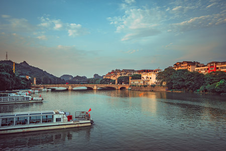 Guilin, China - August 2019 : Barges docked on the riverside with arched road bridge over magnificent Li River in the background, Guilin town, Guangxi Provinceのeditorial素材