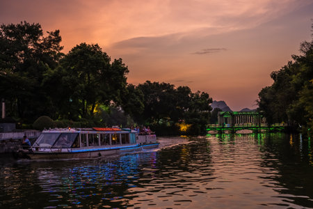 Guilin, China - August 2019 : Sightseeing tour boat ferry carrying tourists sailing in front of Crystal glass bridge on the Shan Lake, Guilin town, Guangxi Provinceのeditorial素材