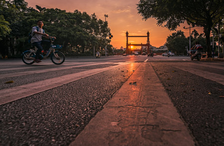 Guilin, China - August 2019 : Chinese Man riding on his bicycle behind zebra pedestrian crossing on Sanduo Lu street at dusk, Guangxi Provinceのeditorial素材