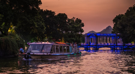 Guilin, China - August 2019 : Sightseeing tour boat ferry carrying tourists sailing in front of Crystal glass bridge on the Shan Lake, Guilin town, Guangxi Provinceのeditorial素材
