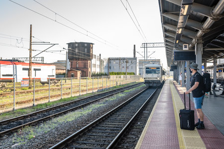 Bydgoszcz, Poland - August 2020 : Middle aged male man wearing protective face mask, pulling a wheeled luggage trolley standing alone on an empty platform awaiting arrival of a scheduled train, traveling in the time of covid19 pandemicのeditorial素材