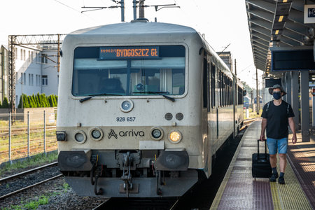 Bydgoszcz, Poland - August 2020 : Middle aged male man wearing protective face mask, pulling a wheeled luggage trolley standing alone on an empty platform awaiting arrival of a scheduled train, traveling in the time of covid19 pandemicのeditorial素材