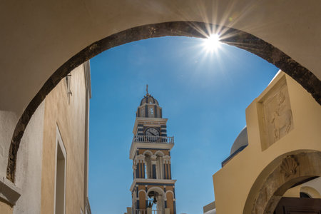 Bell tower with clock of Catholic Cathedral Church of Saint John the Baptist in Fira seen through the arched door passage, Santorini island, Cyclades, Greeceの写真素材