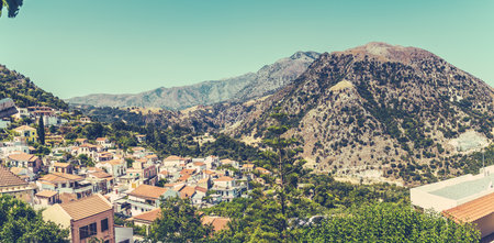 A panoramic shot of buildings with a mountain covered with green trees in the background on a sunny...