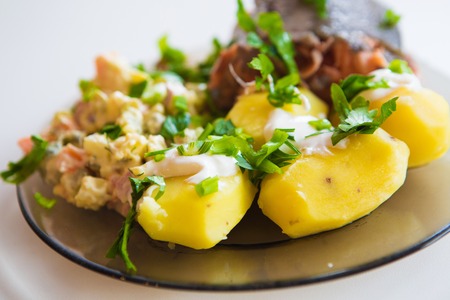 Boiled potatoes under sour cream, red fish, salad sprinkled with parsley on a plate of dark glassの写真素材