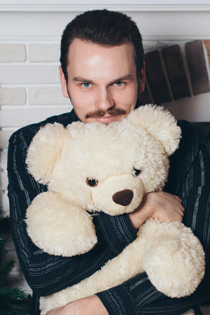 A man in a black shirt hugs a Teddy bear. Beautiful brunette holding a toyの写真素材
