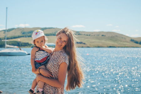 A long-haired woman holds a little child on a lake background.の写真素材