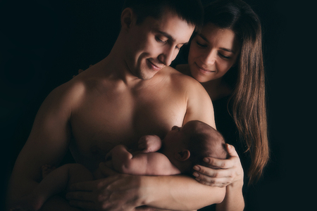 newborn baby lying on the hands of parents on a black background.の写真素材