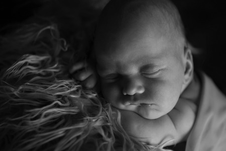 newborn baby lying on a white and black background. Imitation of a baby in the womb. beautiful little child sleeping lying on her tummy. Portrait of newbornの写真素材