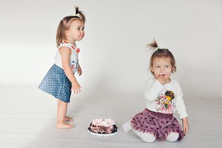 Two little baby girl eating cake isolated white background. children's fashionの写真素材