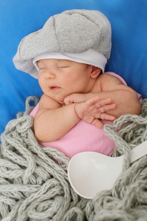 A little child in a grey cap lies witn a spoon on a blue backgroundの写真素材
