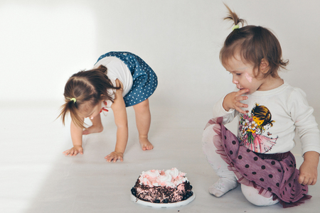 Two little baby girl eating cake isolated white backgroundの写真素材