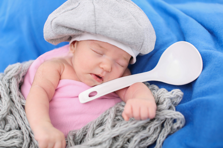 A little child in a grey cap lies witn a spoon on a blue backgroundの写真素材