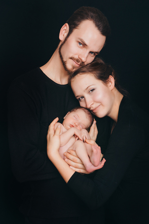 newborn baby lying on the hands of parents on a black background.の写真素材