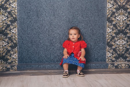 A little girl in red and blue clothes sitting on the floorの写真素材