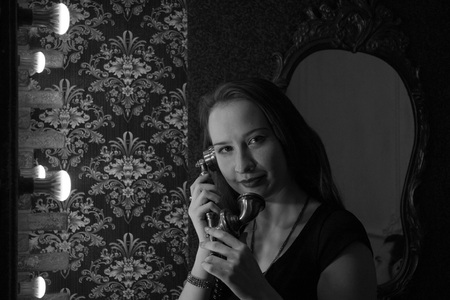 portrait of a female face closeup. The girl smiles and holds up the old phone to the ear on the background of walls with muralsの写真素材