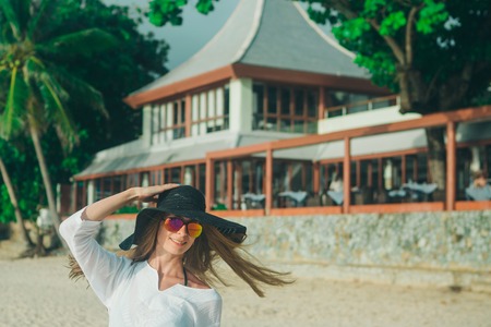 handsome girl with glasses and hat on the beach background. Portrait of a woman in white clothes and balck hatの写真素材