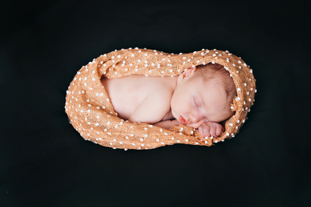 A little child in a beige diaper lies on a black backgroundの写真素材