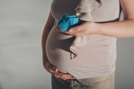 pregnant woman holding hands with booties around the belly on belly on a white backgroundの写真素材