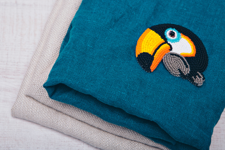 fabric texture as background. Blue and grey flax. Item of clothing close-up. bird Toucan made of beads and a lightning strike.. Symbol on blue backgroundの写真素材