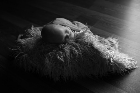 newborn baby lying on a white and black background. Imitation of a baby in the womb. beautiful little child sleeping lying on her tummy. Portrait of newbornの写真素材