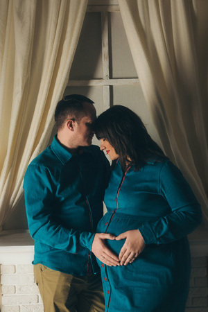 pregnant woman and man holding hands heart shaped on belly on a white backgroundの写真素材