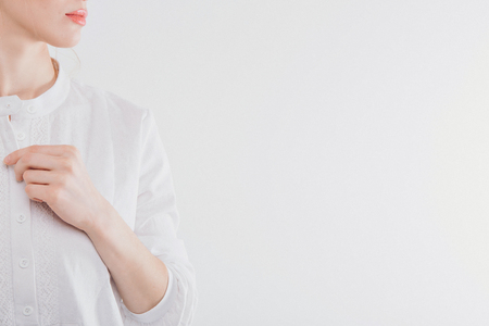 cropped photo: girl holding her hand near her face. Model posing in a white cloth. Item of clothing close-upの写真素材