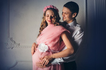 Family portrait: the husband embraces the pregnant wife in pink dress. pregnant couple in love. fashion fro pregnant woman and familyの写真素材