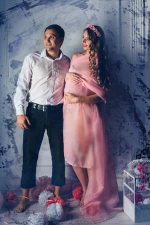Family portrait: the husband embraces the pregnant wife in pink dress. pregnant couple in love. fashion fro pregnant woman and familyの写真素材