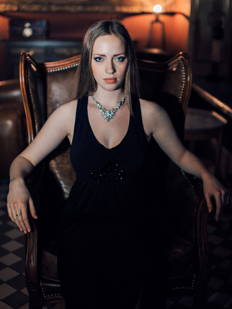 beautiful girl in a long black dress sitting in a chairの写真素材