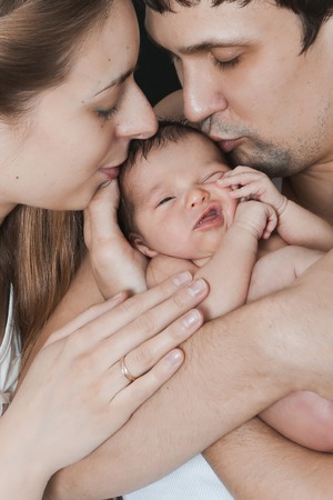 newborn baby lying on the hands of parents on a black background. Mother and father kiss daughterの写真素材