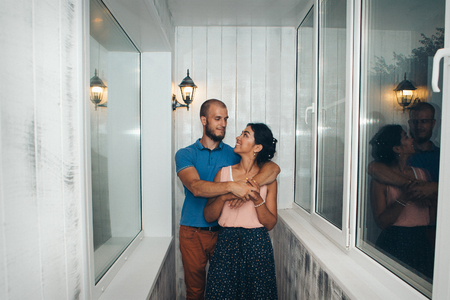 Family portrait of husband and wife. The pair on the balcony. European hugs Asian. Man and woman smilingの写真素材