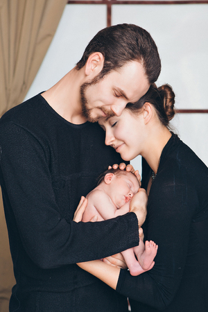 newborn baby lying on the hands of parents on a black background.の写真素材