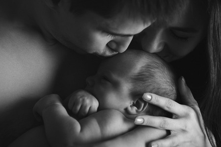 newborn baby lying on the hands of parents on a black background. Man and woman kiss sonの写真素材