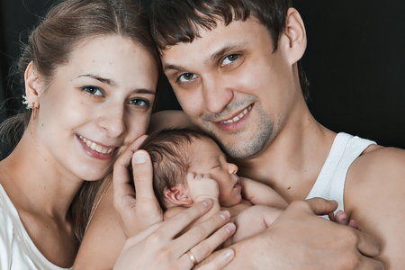 newborn baby lying on the hands of parents on a black background.の写真素材