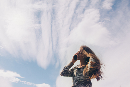 silhouette of a girl talking on the phone against the clouds. Woman posing for the camera against the skyの写真素材