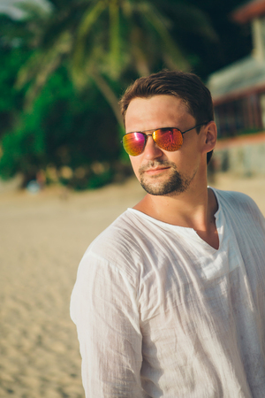 Handsome guy with glasses on the beach background. Portrait of a man in white clothesの写真素材
