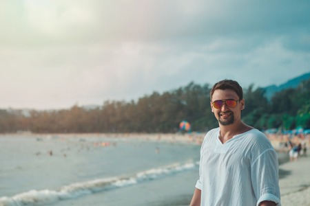 Handsome guy with glasses on the beach background. Portrait of a man in white clothesの写真素材