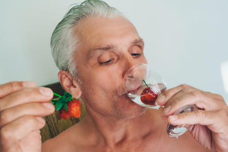 Portrait of a man with a glass and strawberries. pensioner drinks water with fruitの写真素材