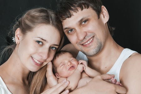 newborn baby lying on the hands of parents on a black background.