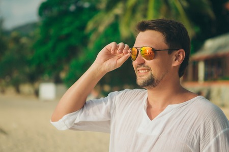 handsome guy with glasses on the beach background. Portrait of a man in white clothesの写真素材