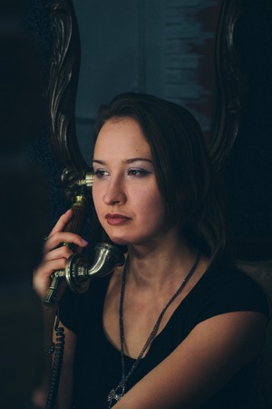 portrait of a female face closeup. The girl smiles and holds up the old phone to the ear on the background of walls with muralsの写真素材