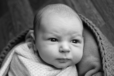Portrait a little child in a cap lies on a basket. Face of newborn