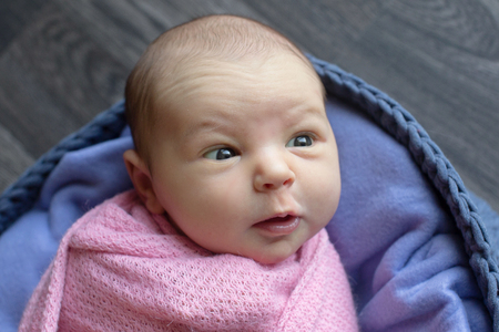 A little child in a pink cap lies on a blue and grey background. Portrait of newbornの写真素材
