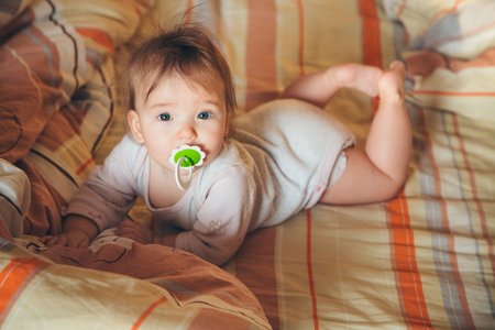 a small child with a pacifier crawling on the bedの写真素材